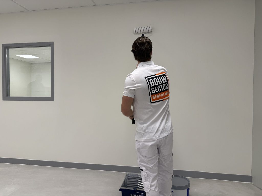 Schilder van Bouwsector Nederland rolt een witte muur, met de verfbak aan zijn voeten
